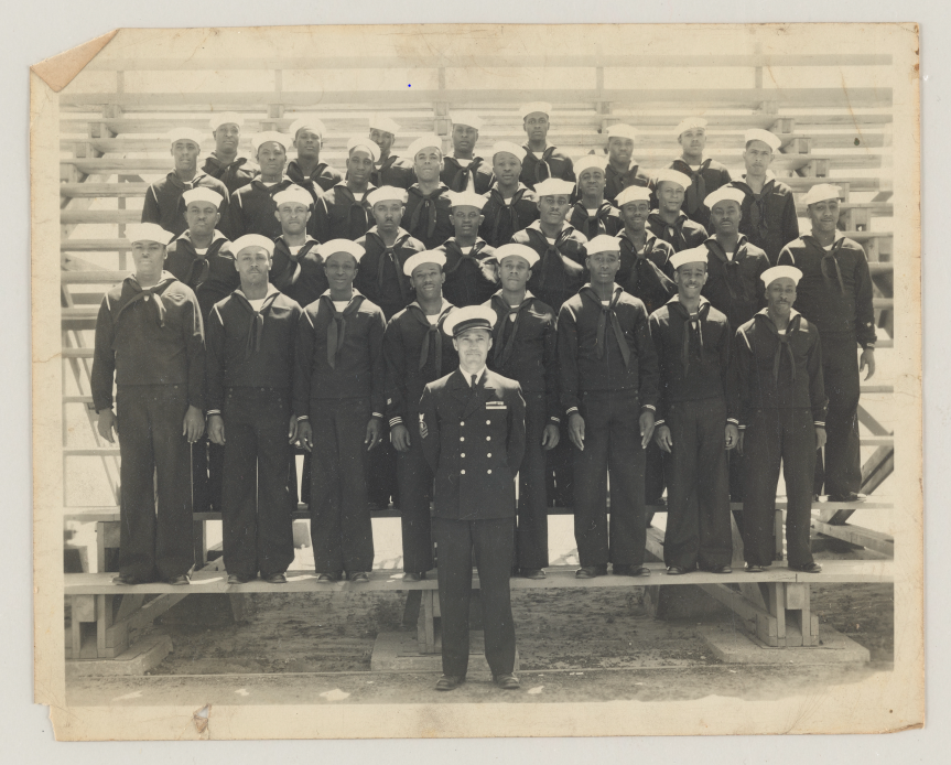 About 30 African American "Seabees" stand in row formation for their photograph. A white lieutenant colonel stands in front of them.