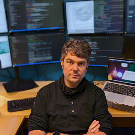 Dan Runfola seated in front of multiple computer displays