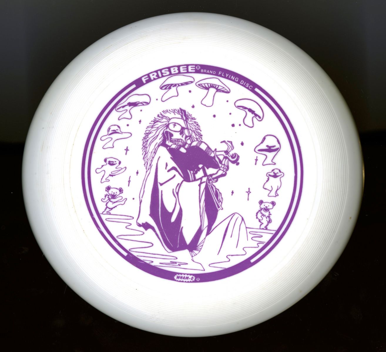 White frisbee with a purple graphic reminiscent of the album cover of the Grateful Dead's album "Blues for Allah." Dancing bears, mushrooms, and stars line the perimeter of the disc's design.