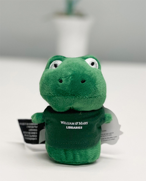 Green plush frog wearing a green t-shirt with the W&M Libraries logo