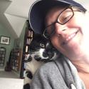 Gina - a dark haired woman in a baseball cap - and a black and white cat cuddling