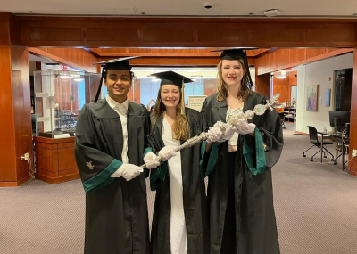Three students in cap and gowns holding the college mace